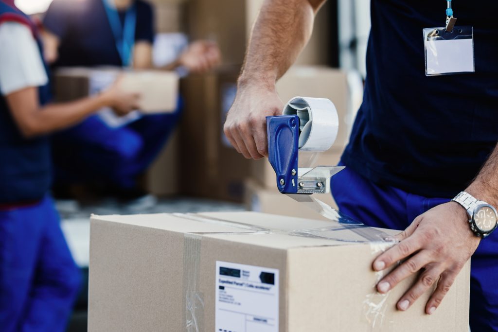 closeup delivery man closing carboard box with tape while preparing packages shipment